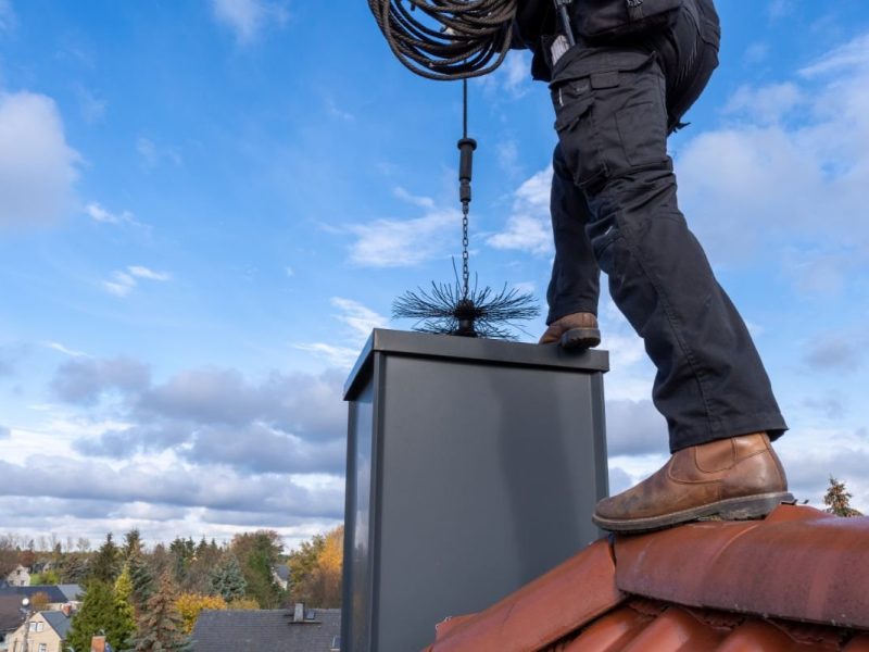 Professional chimney sweep cleaning a chimney flue from the roof